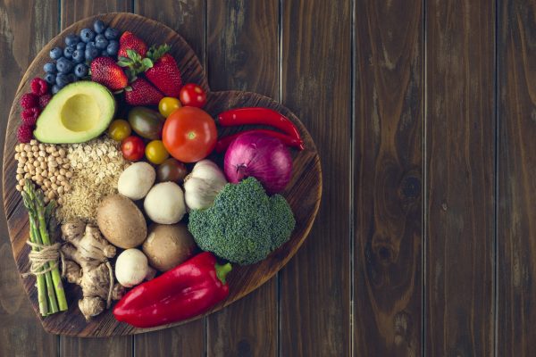 Healthy food on a heart shape cutting board. Love of food concept with fruit, vegetables, grains and high fibre foods. Rustic wood textures
